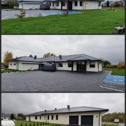 Nowoczesny parterowy budynek z białymi ścianami i ciemnym dachem, otoczony brukowanym podjazdem i trawnikiem, z widocznymi flagami reklamowymi i zaparkowanym vanem.