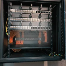 Panel krosowniczy z ponumerowanymi portami, okablowanie w szafie rack, widoczne przewody pomarańczowe i żółto-zielone.