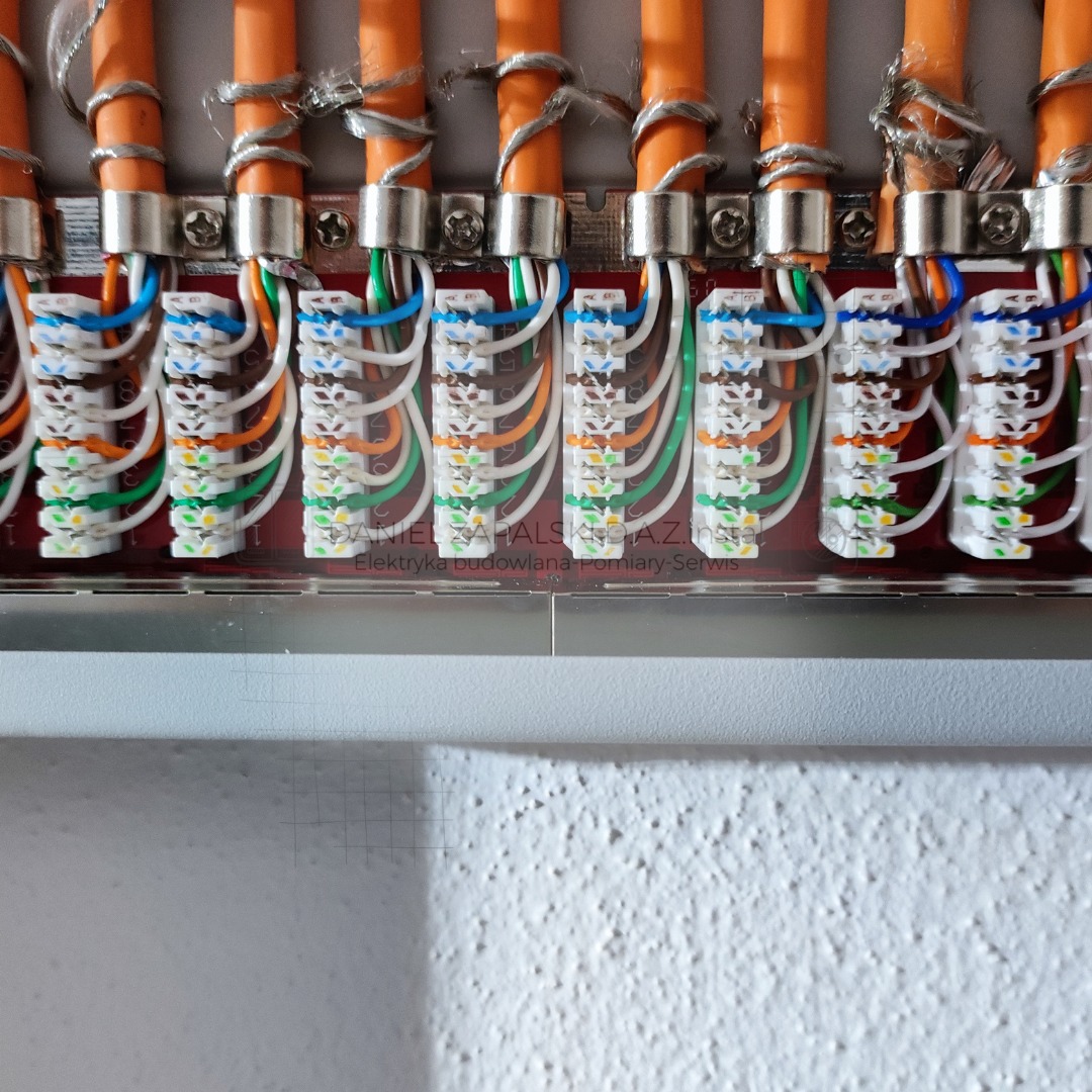 Szereg pomarańczowych kabli sieciowych zakończonych złączami w skrzynce rozdzielczej, widoczne kolorowe przewody wpięte w złącza.