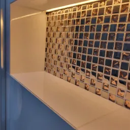 Narożna wnęka z półką, wyłożona mozaiką w odcieniach brązu i szarości, oświetlona listwą LED od góry.