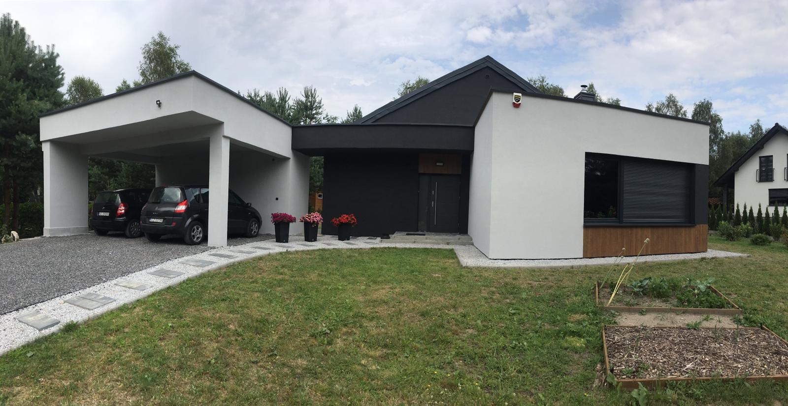Nowoczesny dom jednorodzinny z płaskim dachem, białymi ścianami i czarnymi elementami wykończeniowymi, garażem z dwoma samochodami i zadbanym trawnikiem.