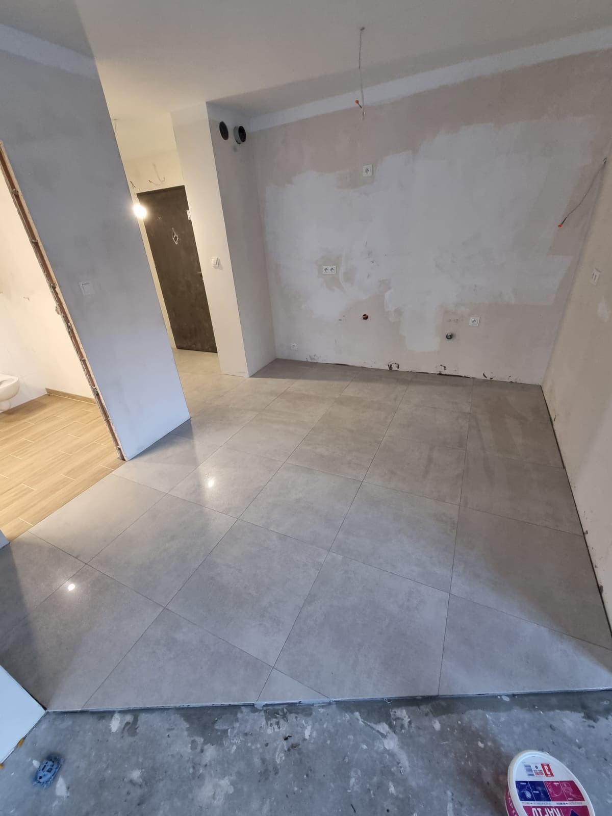 Ułożone szare płytki podłogowe w trakcie remontu mieszkania w Szczekocinach, widoczne niedoskonałości na ścianach przygotowanych do dalszych prac, w tle fragment łazienki z beżowymi płytkami.