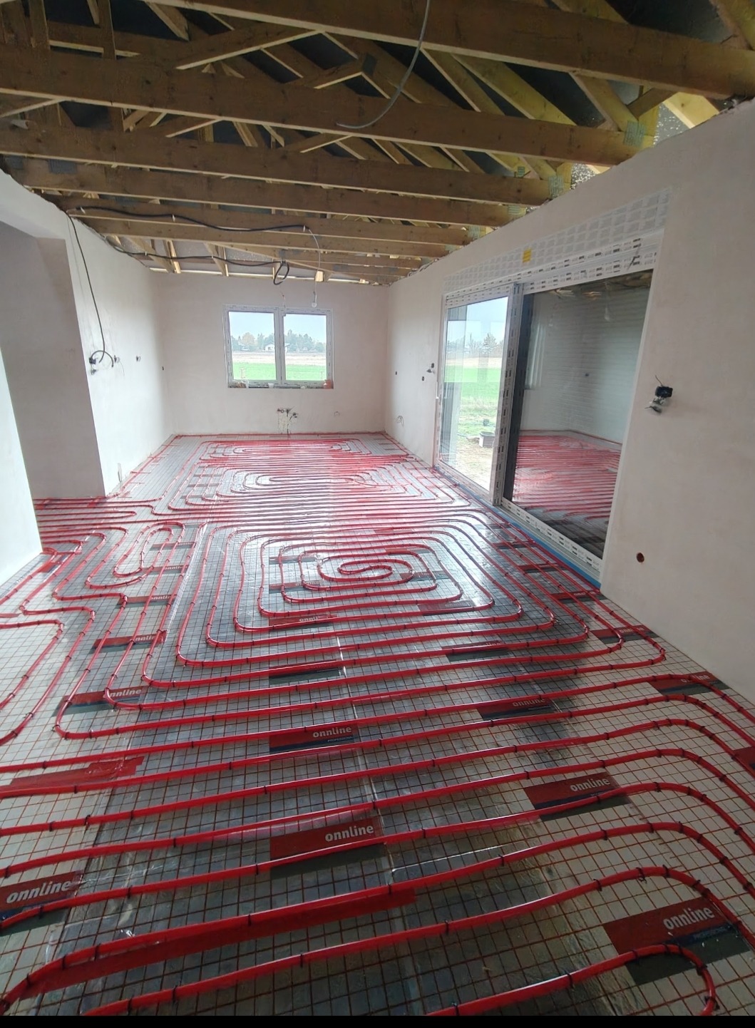 Czerwone rury ogrzewania podłogowego ułożone w nowym domu, widoczne okno i surowy strop. Instalacja przed wylaniem posadzki, widok z góry.