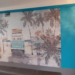 ŚwieżoMalowane24 - Malowidło ścienne przedstawiające plażowy motyw z palmami, surferami, turkusowym vanem z deskami surfingowymi na dachu, oraz drogowskazami do różnych miast świata, w tym Miami, Los Angeles...