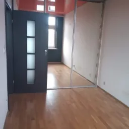 Wnętrze pokoju po remoncie: świeżo ułożona podłoga z paneli, pomalowany sufit na pomarańczowo i przesuwne drzwi do szafy wnękowej.