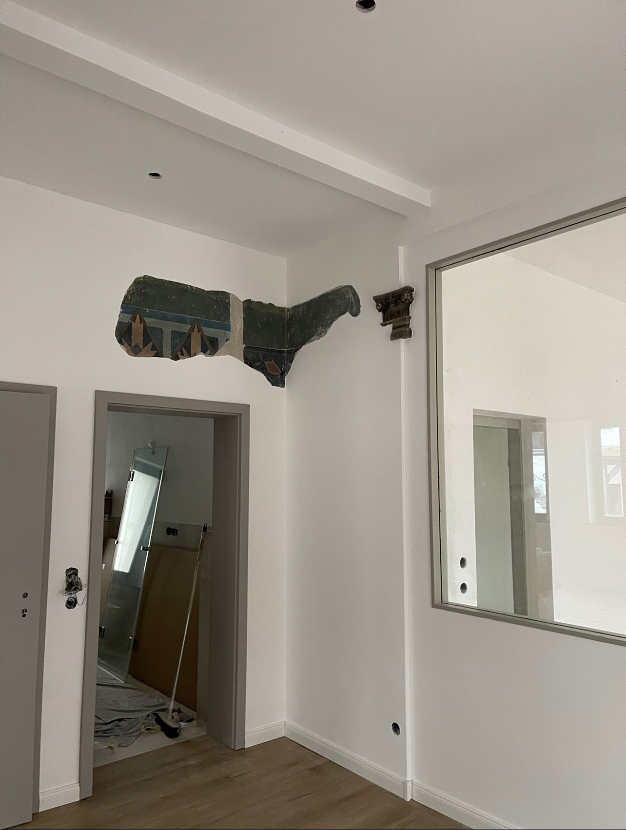 Fragment starego malowidła ściennego z motywami architektonicznymi, odspojony od ściany w trakcie remontu, obok fragment dekoracyjnej kolumny, widoczne przygotowania do prac wykończeniowych.