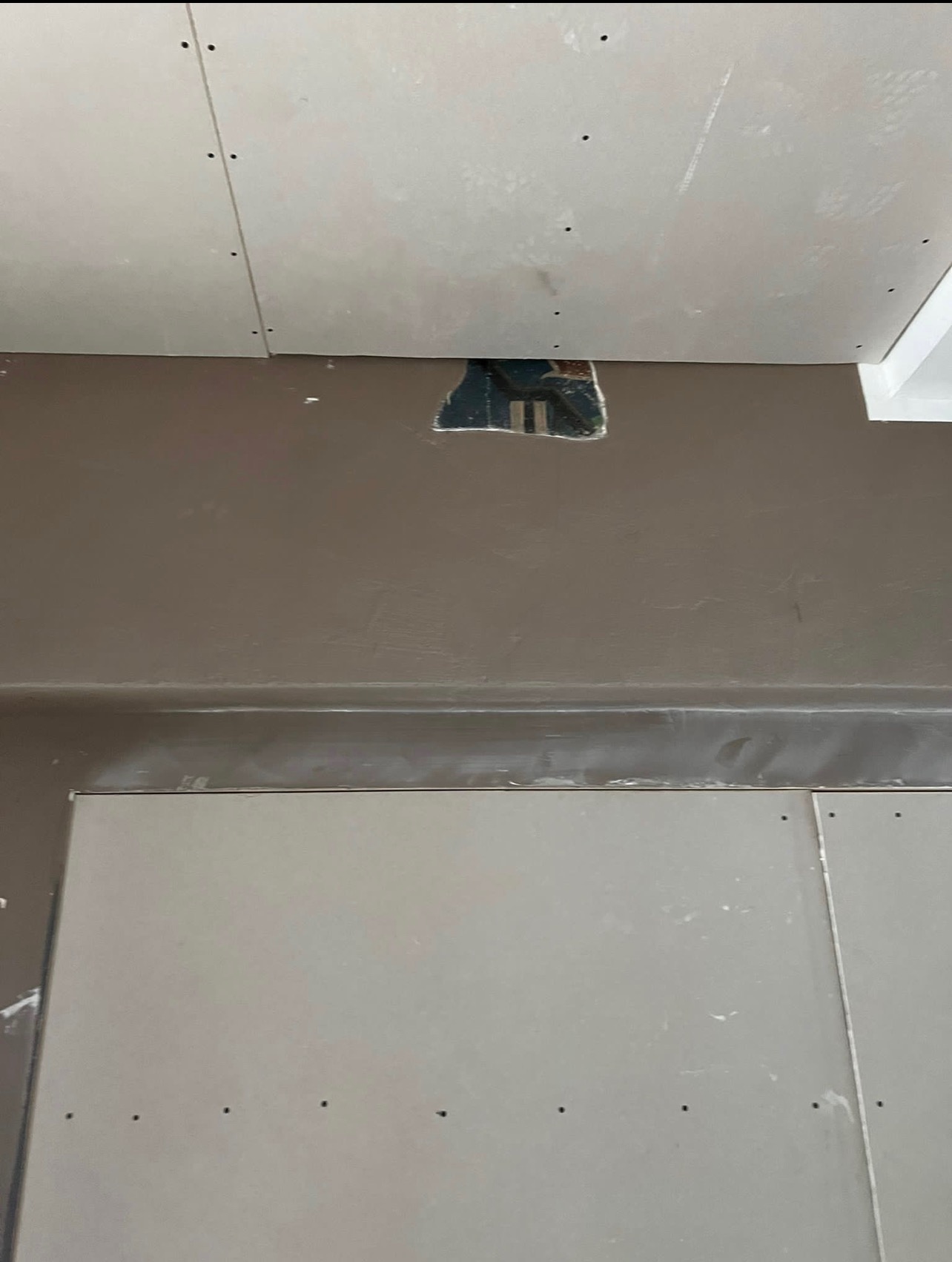 Ściana i sufit w trakcie remontu: szpachlowana ściana w kolorze taupe, sufit z płyt gipsowo-kartonowych z widocznym otworem instalacyjnym.