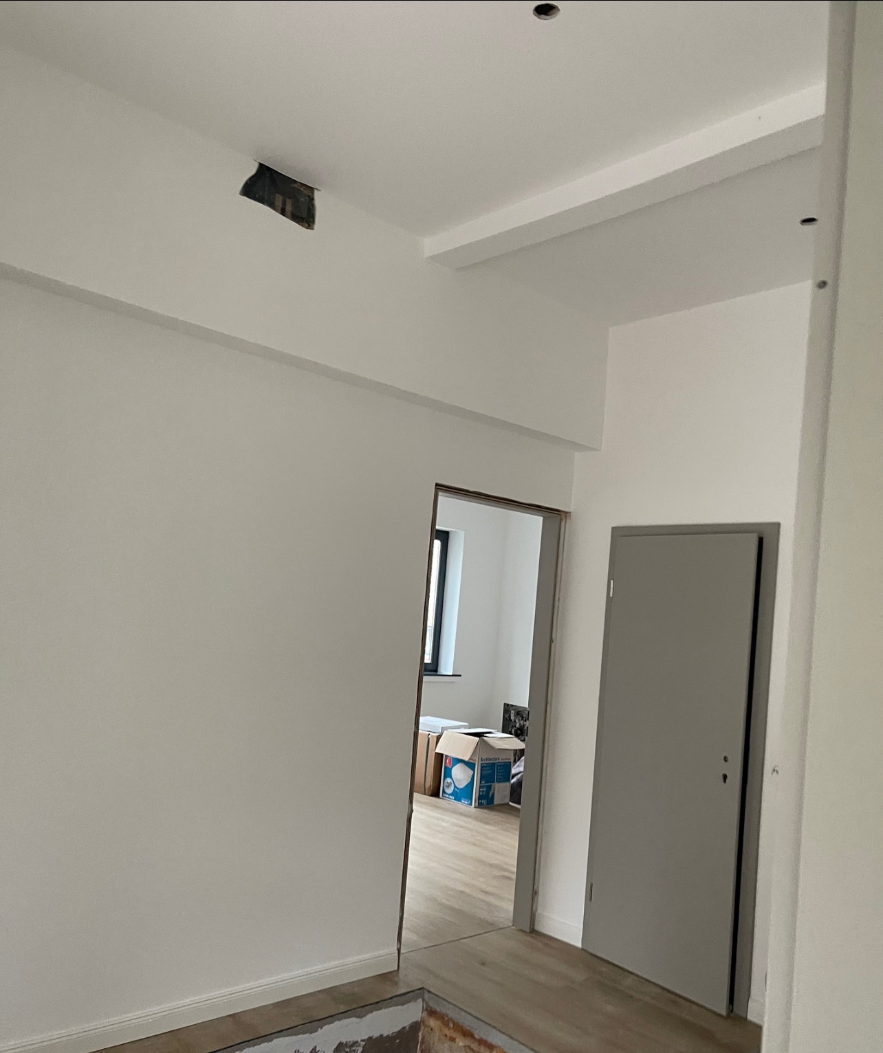 Wnętrze w trakcie prac wykończeniowych: świeżo pomalowane na biało ściany, widoczne fragmenty podłogi przed położeniem paneli, surowy otwór w suficie.