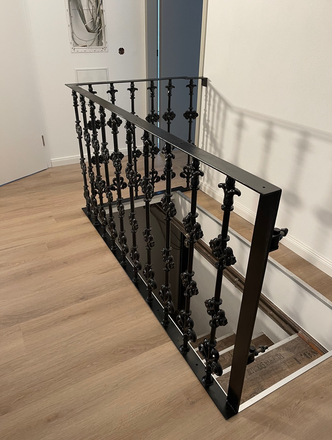 Nowoczesna, czarna balustrada schodowa z ozdobnymi elementami, zamontowana przy zejściu do piwnicy, widoczna na tle jasnego parkietu i białych ścian.