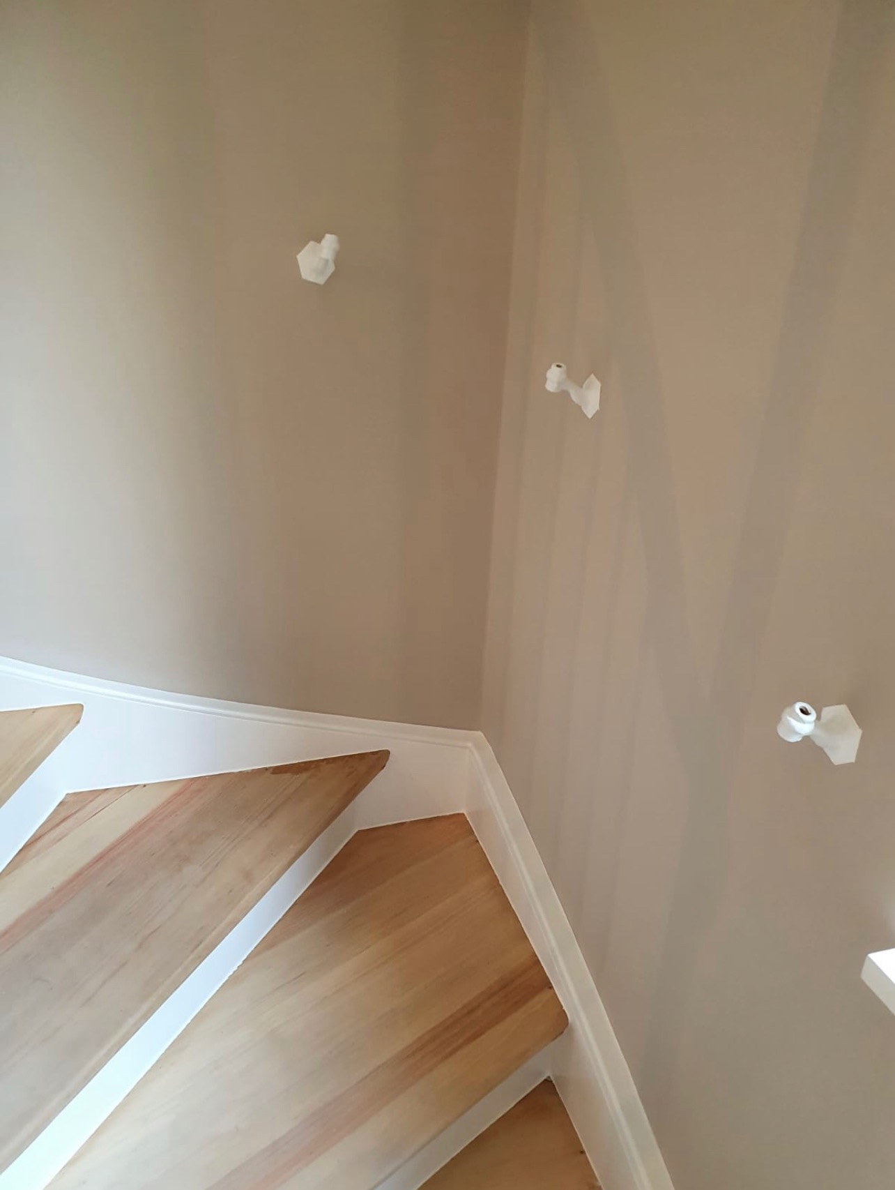 Przygotowanie do malowania: zabezpieczone taśmą malarską ściany w odcieniach beżu, widoczne fragmenty drewnianych schodów z białymi listwami przypodłogowymi.