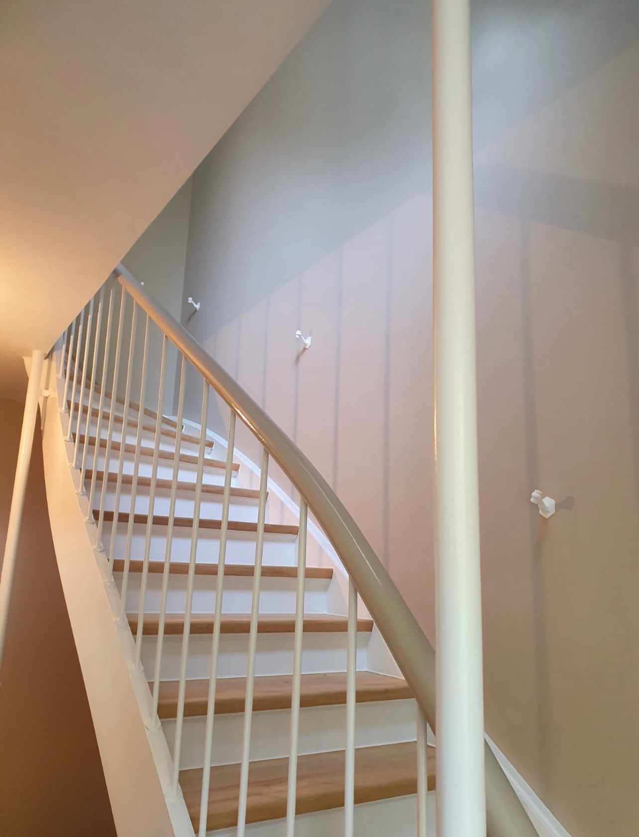 Klatka schodowa po odświeżeniu, z drewnianymi stopniami i pomalowanymi na biało barierkami oraz kremowymi ścianami z widocznymi wieszakami.