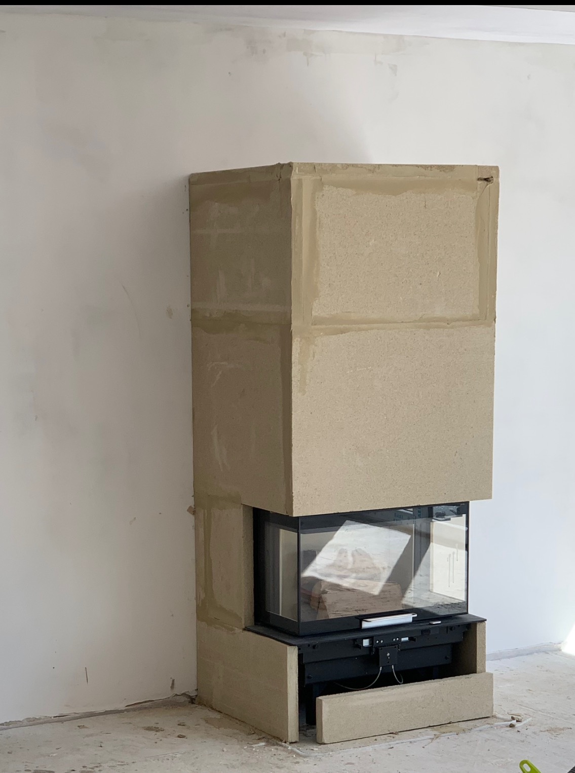 Wnętrze w trakcie remontu: obudowa kominka z płyt gipsowych przed wykończeniem, widoczne łączenia i szpachlowanie, surowy stan ścian w tle.