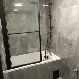 Michał Majcher - Szara łazienka z wanną obudowaną płytkami, czarną kabiną prysznicową i baterią natryskową w stylu retro.