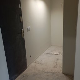 Michał Majcher - Nowoczesne wykończenie przedpokoju z marmurową podłogą, szara, matowa drzwi wejściowe i czarne oświetlenie sufitowe typu spot.