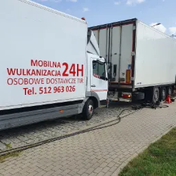 Mobilny serwis wulkanizacyjny 24H przy naczepie TIR, widoczny zapas opon i przewody pneumatyczne na chodniku z kostki.