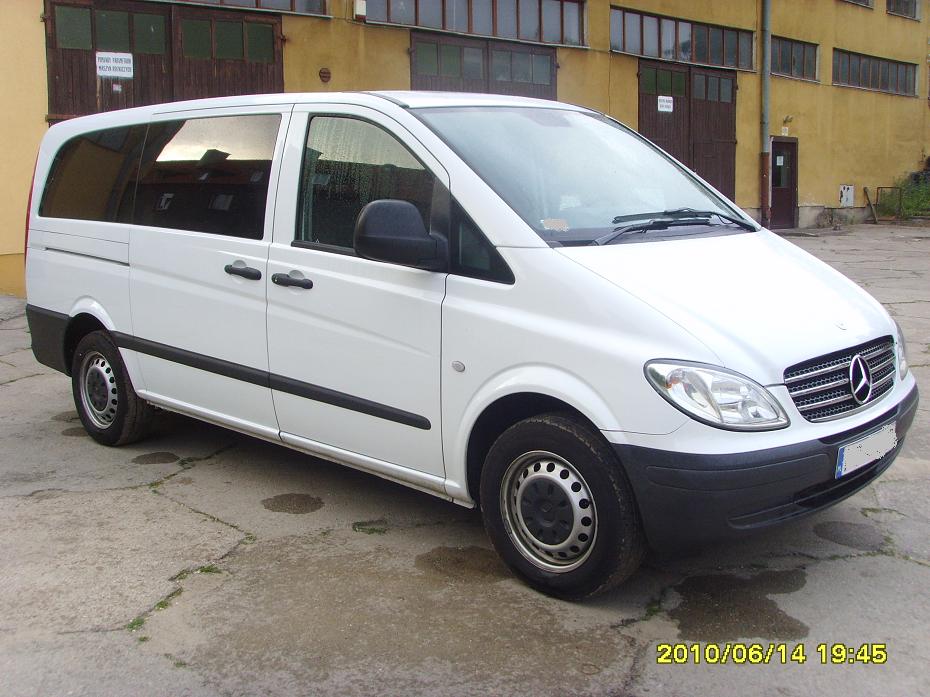 Biały Mercedes-Benz Vito, widok z boku, zaparkowany na betonowym placu przed żółtym budynkiem z ciemnymi bramami garażowymi, data i godzina wykonania zdjęcia widoczne w prawym dolnym rogu.