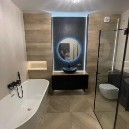 Rembudpro - Nowoczesna łazienka z wolnostojącą wanną, czarną armaturą, okrągłym lustrem z podświetleniem LED i kabiną prysznicową ze szklanymi drzwiami.