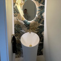 Rembudpro - Nowoczesna łazienka z umywalką na postumencie, lustrem z podświetleniem LED i tapetą w motywy tropikalne, widoczne odbicie osoby robiącej zdjęcie.