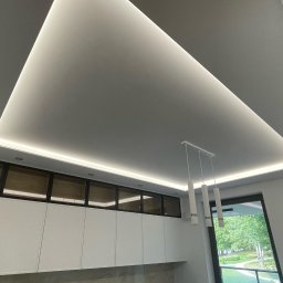 Rembudpro - Nowoczesna kuchnia z podwieszanym sufitem z oświetleniem LED, białymi szafkami i marmurowym blatem, widok z dołu na sufit i oświetlenie.