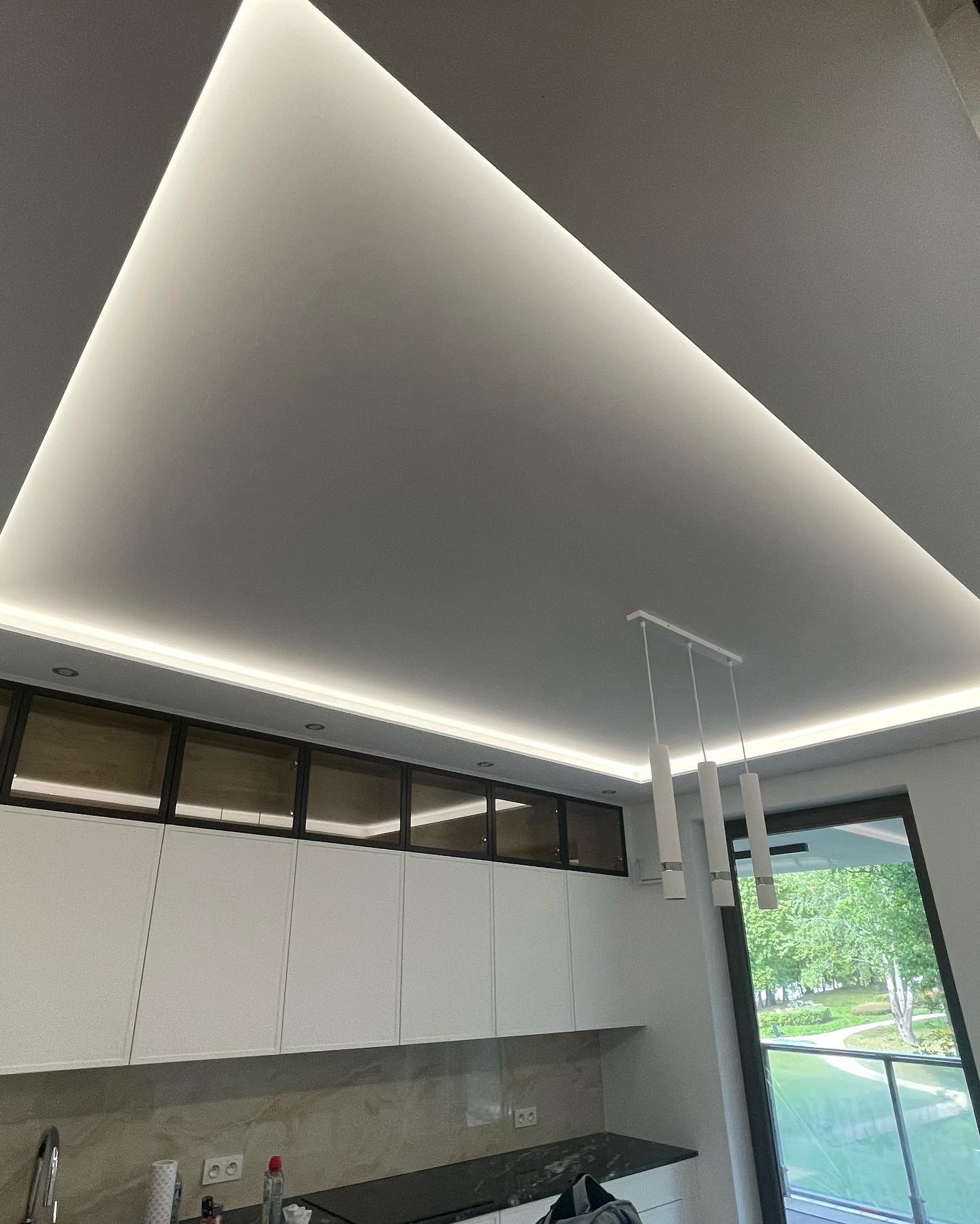 Nowoczesna kuchnia z podwieszanym sufitem z oświetleniem LED, białymi szafkami i marmurowym blatem, widok z dołu na sufit i oświetlenie.