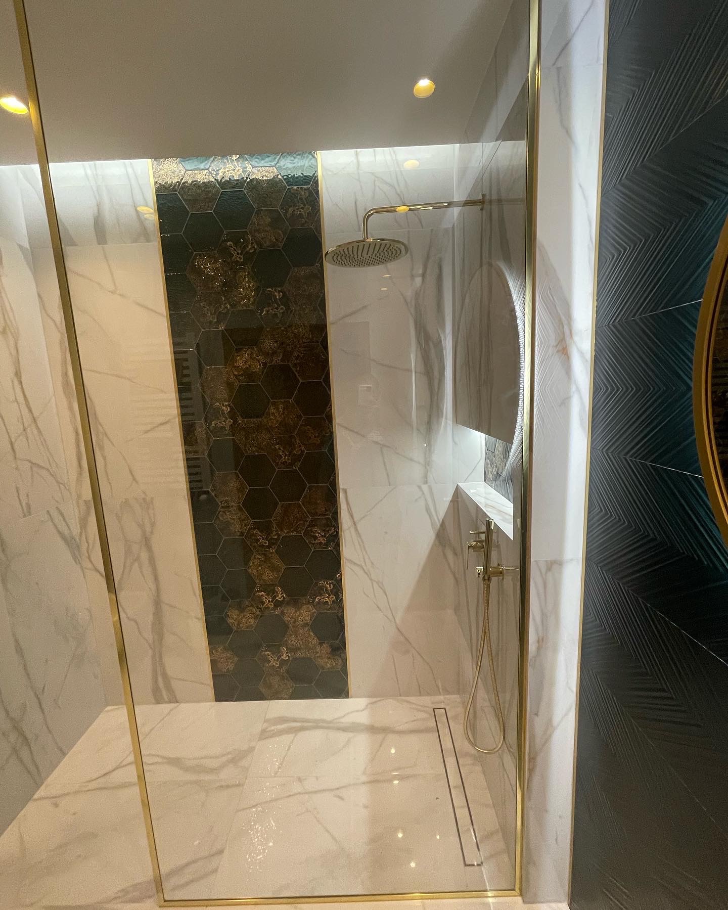 Nowoczesna kabina prysznicowa z marmurowymi płytkami, złotymi detalami i dekoracyjną mozaiką w kształcie heksagonów.