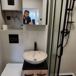 Wiktor Kharchenko usługi budowlane - Nowoczesna łazienka z kabiną prysznicową typu walk-in z czarnymi profilami, marmurową umywalką nablatową na szafce z drewnopodobnymi frontami, toaletą wiszącą i bojlerem elektrycznym; w lustrze...