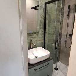 Wiktor Kharchenko usługi budowlane - Nowoczesna łazienka z zielonymi płytkami imitującymi marmur, kabiną prysznicową z czarnymi ramami i umywalką nablatową na szafce z szufladami w kolorze szarozielonym.