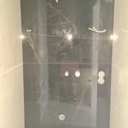 Wiktor Kharchenko usługi budowlane - Ściana łazienki wyłożona płytkami imitującymi czarny marmur z widocznymi otworami na oświetlenie i wystającymi przewodami elektrycznymi przed montażem.