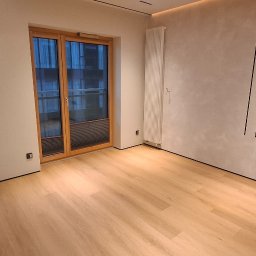 Wiktor Kharchenko usługi budowlane - Jasne panele podłogowe w pokoju z drewnianą stolarką okienną i grzejnikiem na ścianie. Minimalistyczny design wnętrza z elementami dekoracyjnymi.