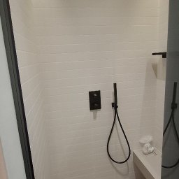 Wiktor Kharchenko usługi budowlane - Nowoczesna kabina prysznicowa z białymi, poziomymi płytkami, czarną armaturą i oświetleniem LED. Minimalistyczny design z ławką i odpływem liniowym.