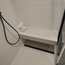 Wiktor Kharchenko usługi budowlane - Nowoczesna kabina prysznicowa z białymi płytkami, siedziskiem i czarną armaturą. Minimalistyczny design, widoczne detale wykończenia.