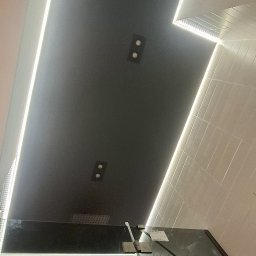 Wiktor Kharchenko usługi budowlane - Nowoczesna łazienka z czarnym sufitem podwieszanym, oświetleniem LED i szklaną kabiną prysznicową. Widok z dołu, podkreślający geometrię i minimalistyczny design.