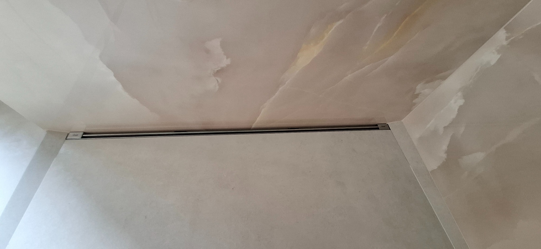 Wykończona łazienka z marmurową teksturą na suficie i ścianach, z widoczną listwą oświetleniową LED zamontowaną w rogu.