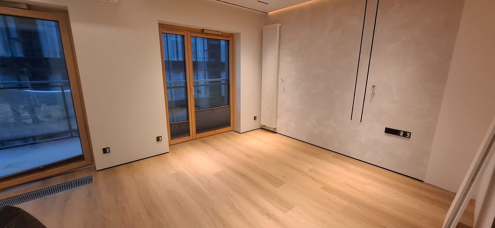 Jasne panele podłogowe w pokoju z drewnianą stolarką okienną i grzejnikiem na ścianie. Minimalistyczny design wnętrza z elementami dekoracyjnymi.