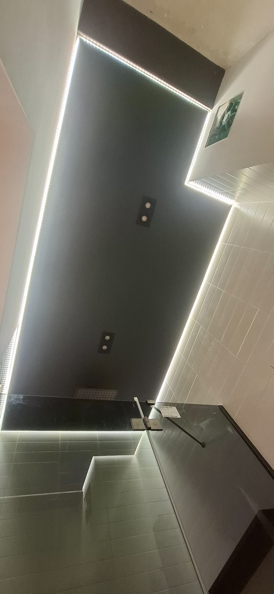 Nowoczesna łazienka z czarnym sufitem podwieszanym, oświetleniem LED i szklaną kabiną prysznicową. Widok z dołu, podkreślający geometrię i minimalistyczny design.