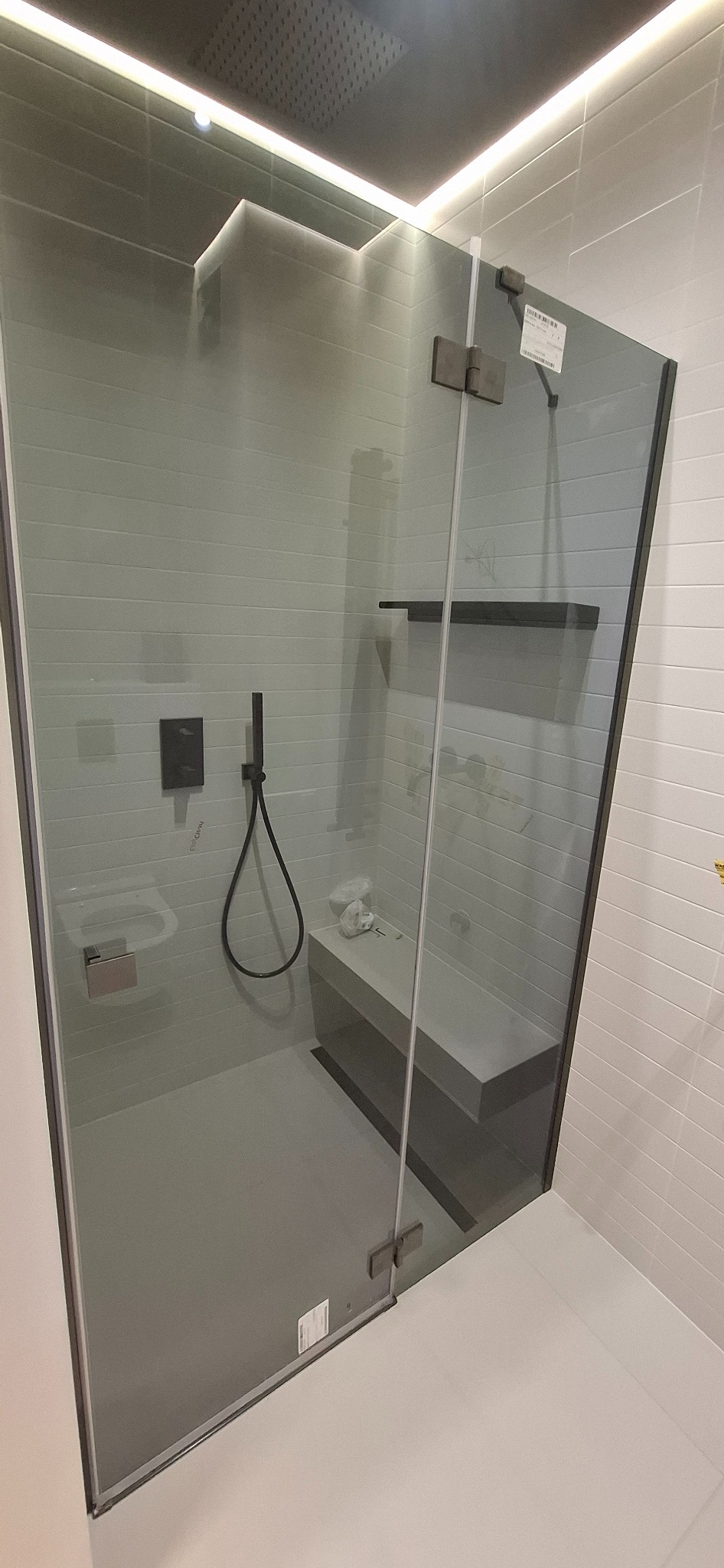 Nowoczesna kabina prysznicowa z grafitowymi elementami, szklanymi drzwiami i subtelnym oświetleniem LED. Widoczna półka i siedzisko wewnątrz kabiny.