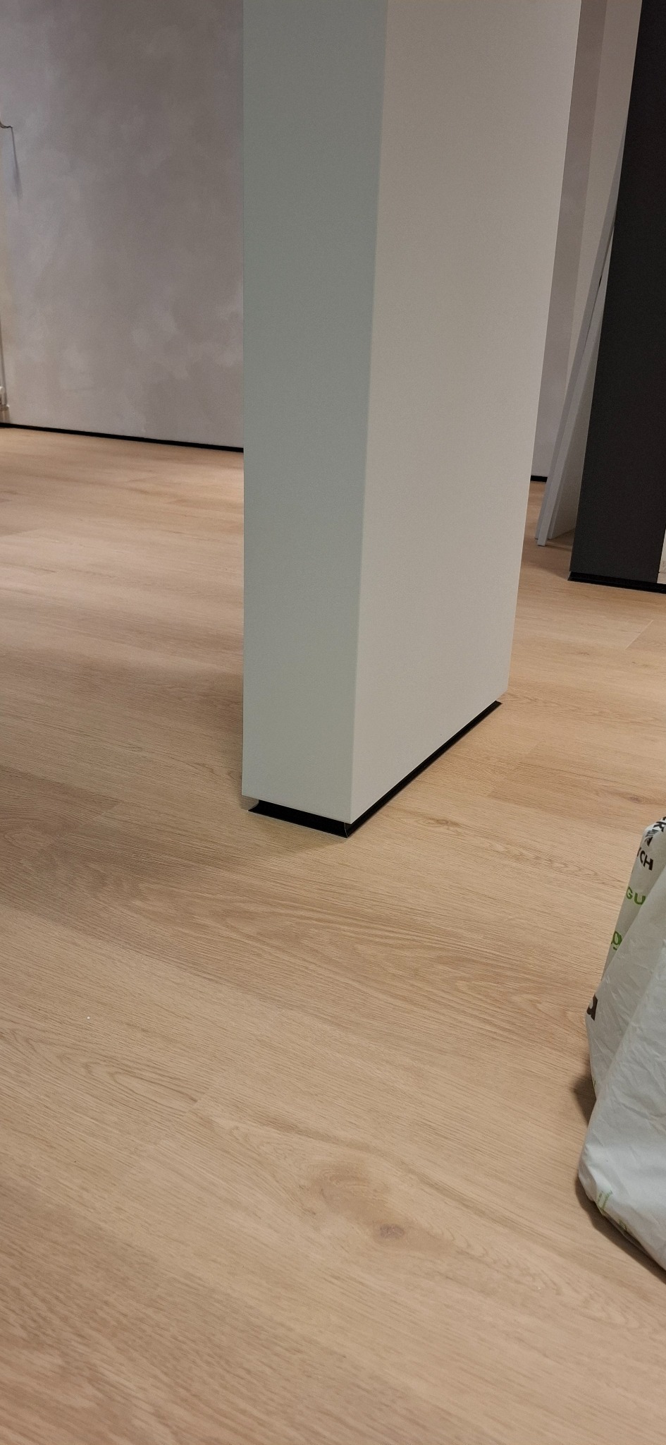 Jasna podłoga z paneli, fragment białej kolumny i ściana w tle. Widoczne detale wykończenia, minimalistyczny styl.