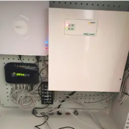 Wnętrze szafy telekomunikacyjnej z zamontowanym rejestratorem Hikvision, routerem BFM24, listwą zasilającą i okablowaniem, widoczne diody sygnalizujące pracę urządzeń.