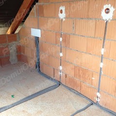 Wnętrze w trakcie prac elektrycznych: przewody prowadzone po ścianie z pustaków ceramicznych, zabezpieczone uchwytami, widoczne puszki instalacyjne w ścianie, podłoga z płyty OSB.