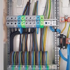 Rozdzielnica elektryczna z precyzyjnie ułożonymi przewodami o różnych kolorach, podłączonymi do listew zaciskowych. Widoczne metalowe szyny montażowe i elementy mocujące. Przewody ułożone...