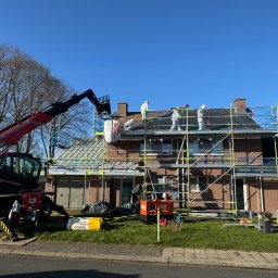 BART-DACH - Pracownicy w kombinezonach na rusztowaniu, demontaż starego pokrycia dachu z pomocą podnośnika teleskopowego, widoczne worki na odpady i materiały izolacyjne Isover