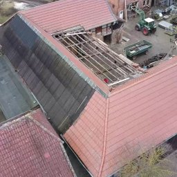 BART-DACH - Widok z góry na częściowo zdjęte pokrycie dachowe z drewnianą konstrukcją więźby, obok budynek z dachem pokrytym czerwoną dachówką, na podwórzu traktor i przyczepy.