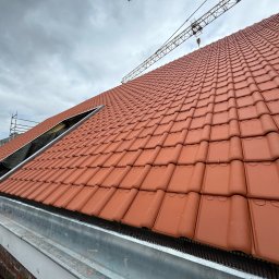 BART-DACH - Nowe, czerwone dachówki ceramiczne ułożone na dachu, z widocznym fragmentem rusztowania i żurawiem w tle, pod pochmurnym niebem.