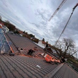 BART-DACH - Ekipa dekarzy pracuje na dachu z ciemnej dachówki ceramicznej, widoczny dźwig budowlany i drabina, pochmurne niebo w tle.