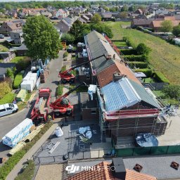 BART-DACH - Widok z lotu ptaka na kompleksową renowację dachów szeregowców. Robotnicy na rusztowaniach i dachach, dźwigi podnoszące materiały. Widoczne etapy prac: stare dachówki, nowa membrana i zielone...