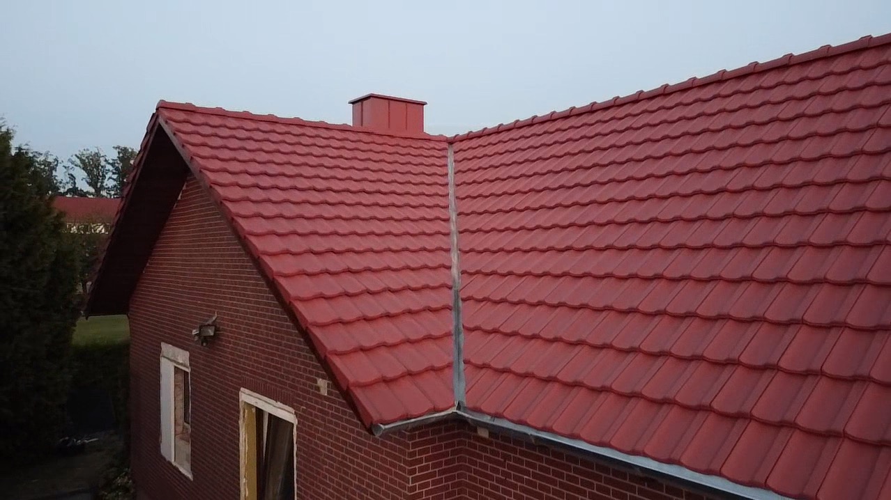 Czerwona dachówka ceramiczna na dachu domu z cegły, widoczny komin i okno w stanie surowym.