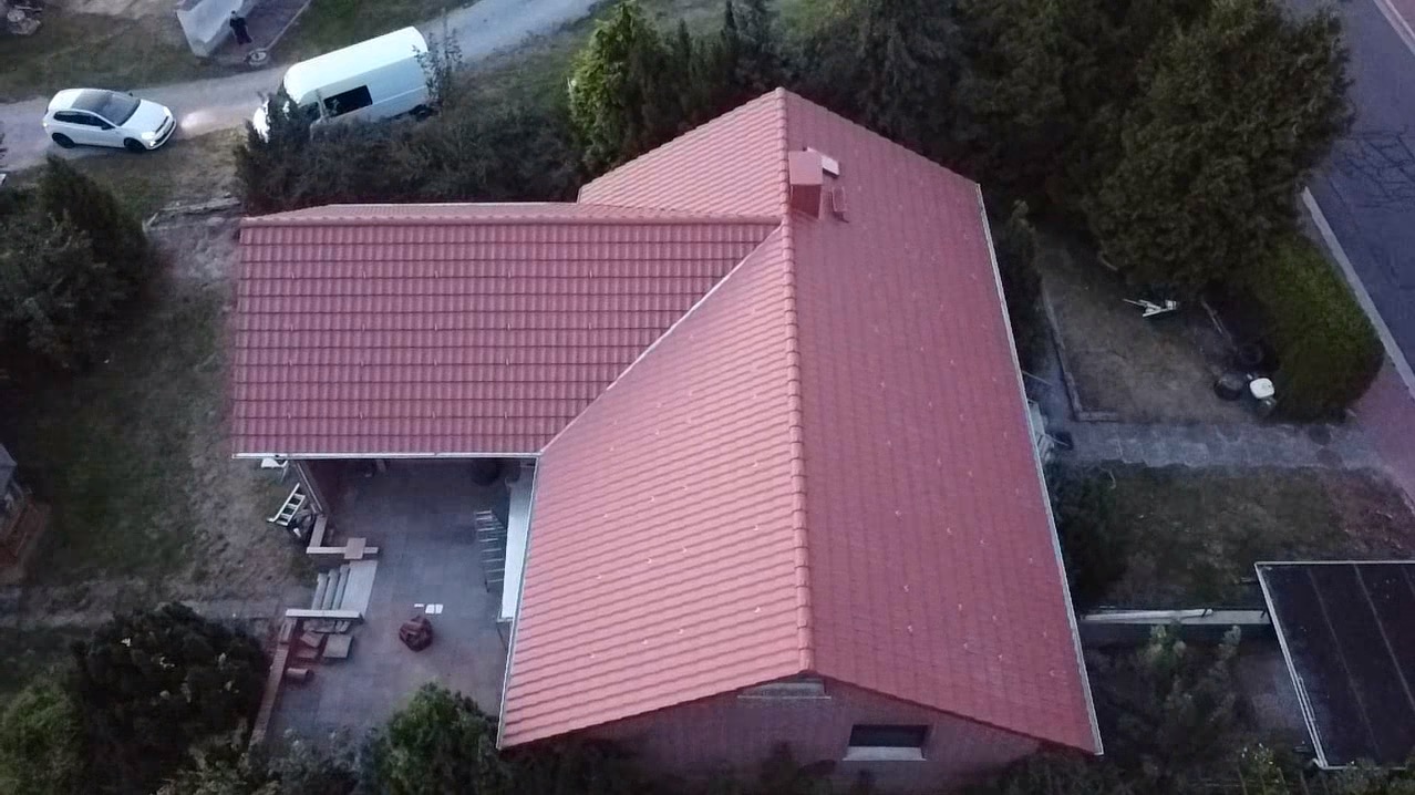Widok z góry na dom z nowym, czerwonym dachem z dachówki ceramicznej; na podwórku zaparkowane samochody i ustawiona drabina.