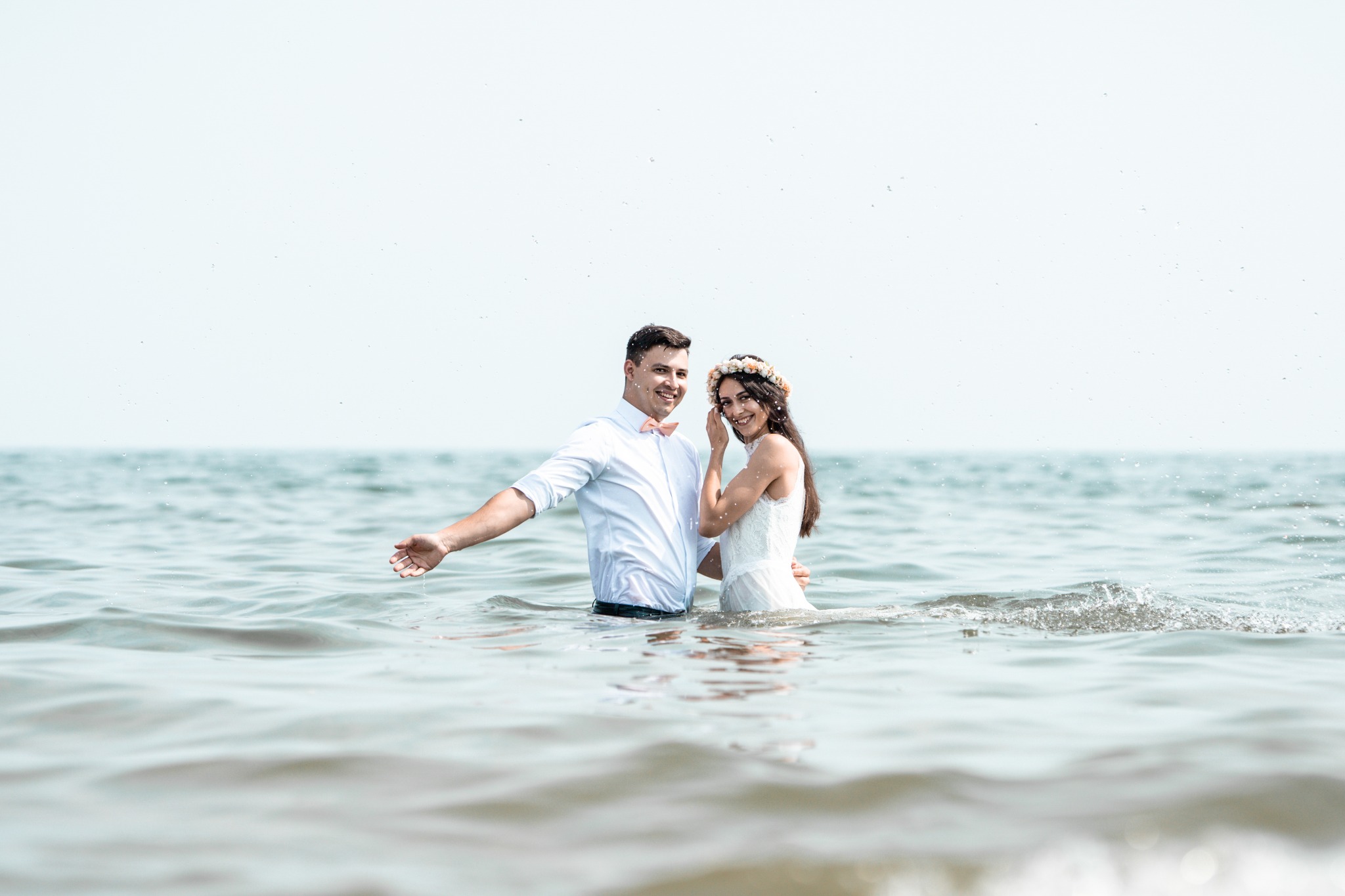 Para młoda w wodzie podczas sesji ślubnej w Lublinie, panna młoda ma wianek na głowie, a pan młody różową muszkę.