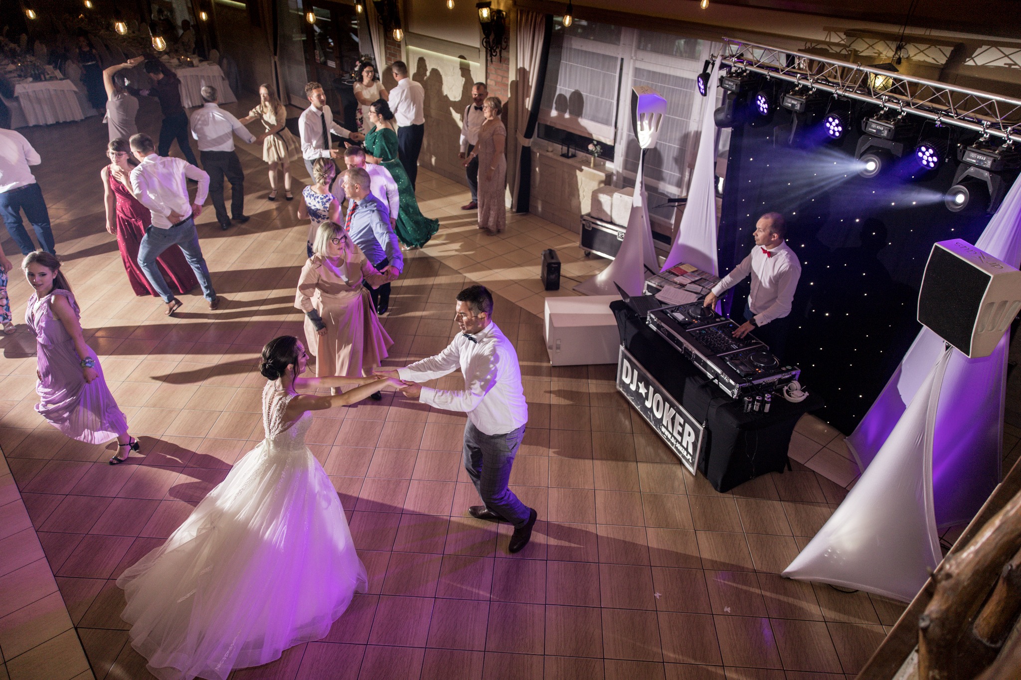 Para młoda tańczy na parkiecie podczas wesela, widok z góry na salę z gośćmi, DJ-em i oświetleniem.