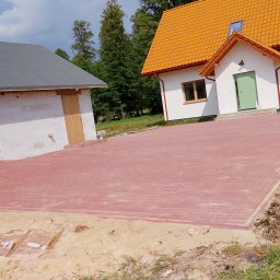 Marcin - Czerwona kostka brukowa ułożona na podjeździe przed nowym domem z pomarańczowym dachem i garażem z białego bloczka. Widoczne fragmenty trawnika i piasku.